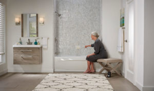 A woman sits at the edge of the bathtub in a spacious remodeled bathroom.