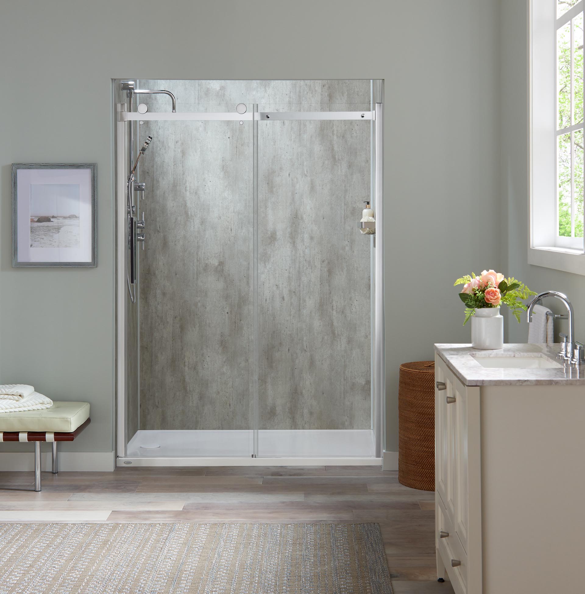 A step in shower has a sliding glass door with exposed rollers and a gray textured wall surround.